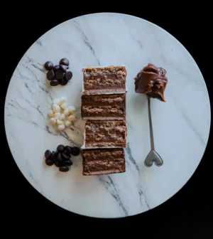 Corte transversal de Alfajores sobre plato de mármol con gotas de chocolate negro y blanco, acompañadas de una cuchara con crema de chocolate.